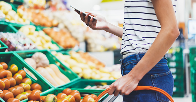 woman shopping for groceries while looking at cell phone