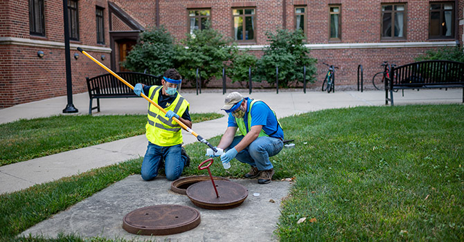 Two workers with the University of Michigan's Environment Health & Safety collect sewage samples from Stockwell Hall in the Hill Neighborhood at U-M's Ann Arbor Campus.