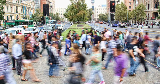 A crowd of people walking across a busy city intersection.