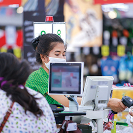 A cashier wearing a mask checks out food items for a customer