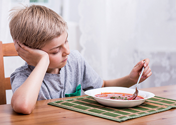 Child apprehensively stirs a bowl of soup