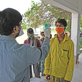 A health screener in India directs a thermometer at a patient