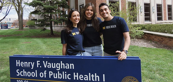 graduating students standing by the school of public health sign