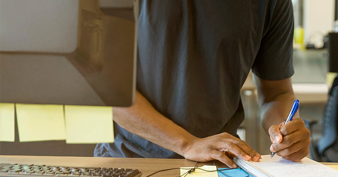 man standing at public computer writing mental health resources on notepad