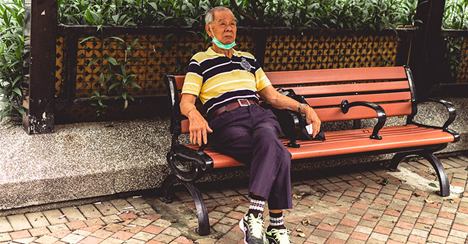 A man sits on a bench with a mask on.