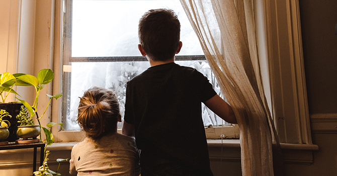 Two young children looking out of a window.