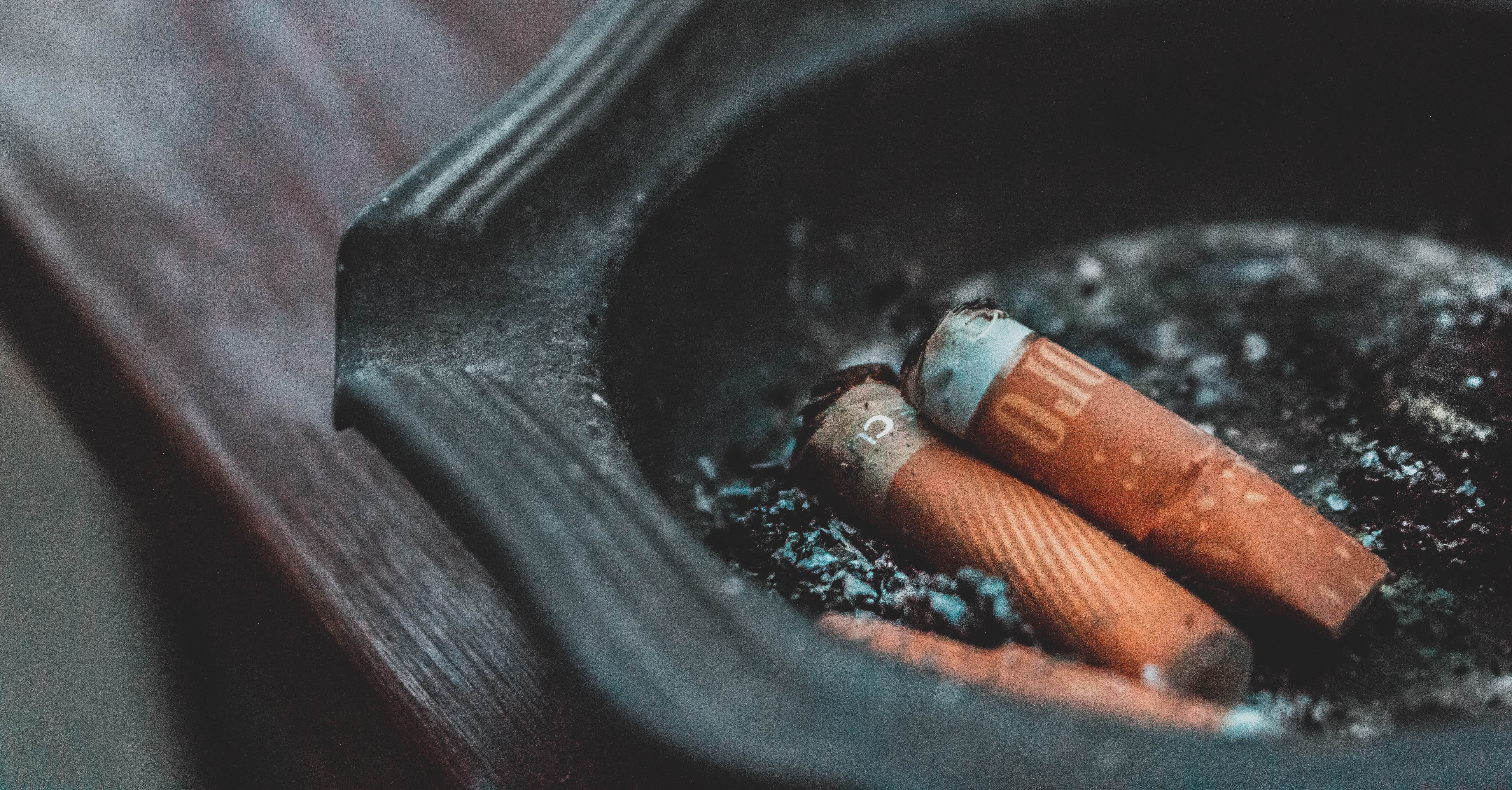 Two cigarettes sit in a black ashtray on a wood surface.