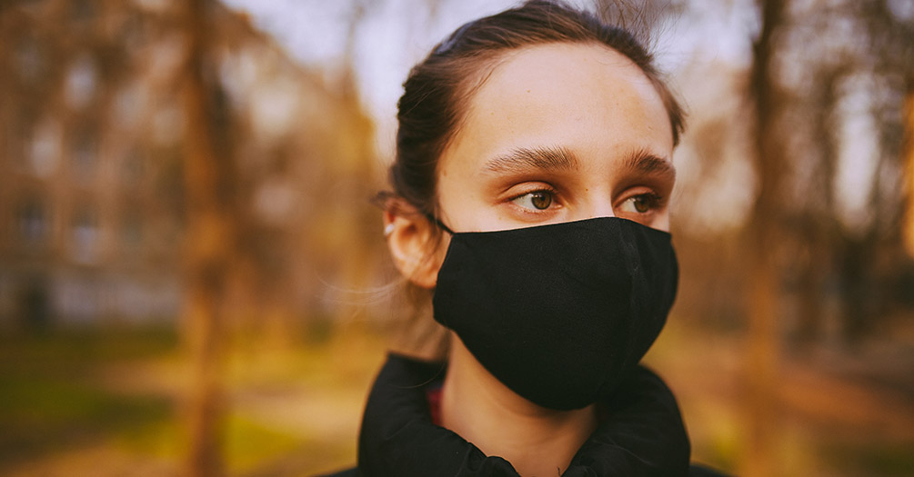 A woman wearing a black mask outdoors.