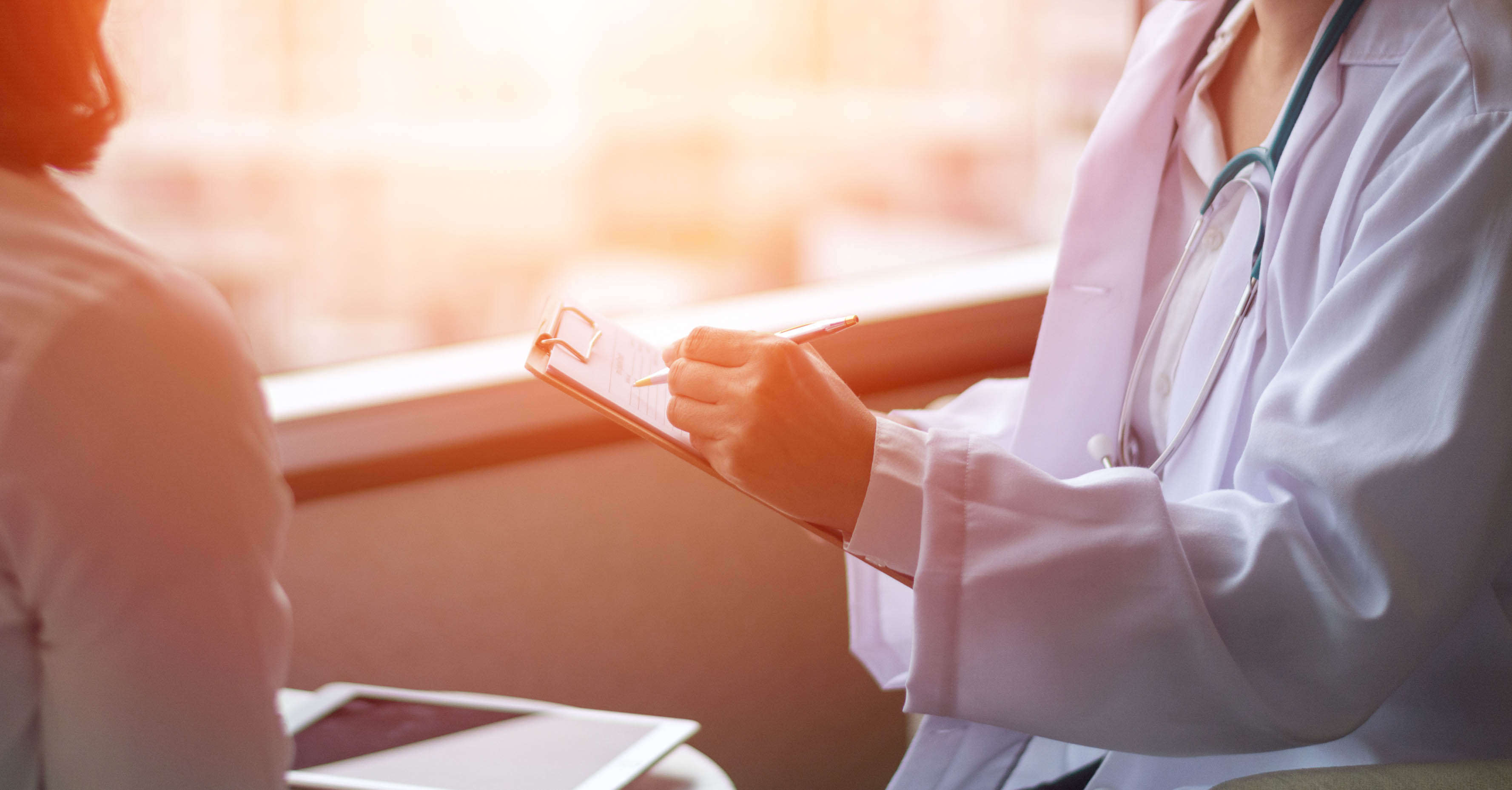 A doctor writes on a clipboard while interviewing a female patient.