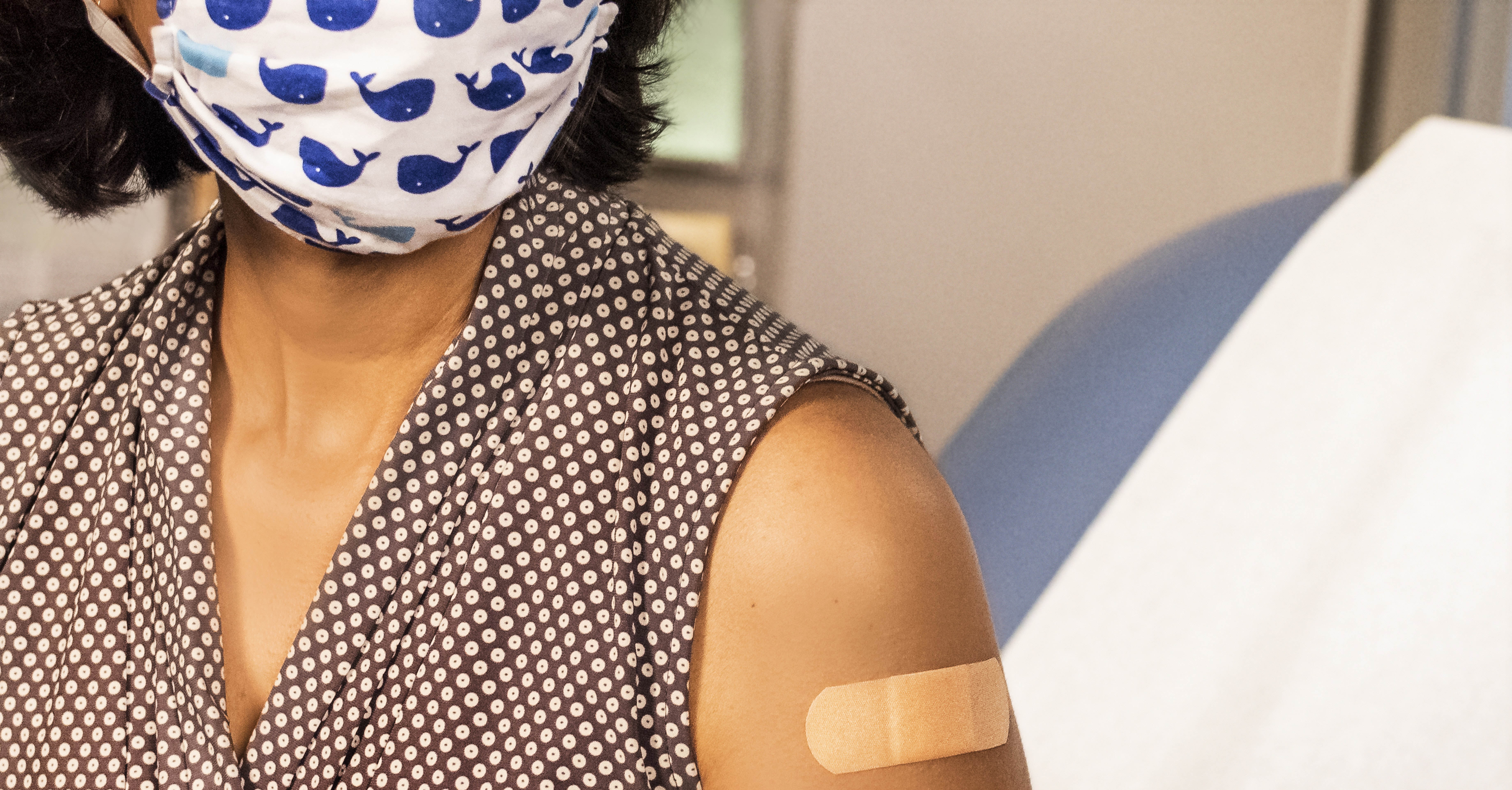 A woman wearing a polka dot top receives a vaccination.