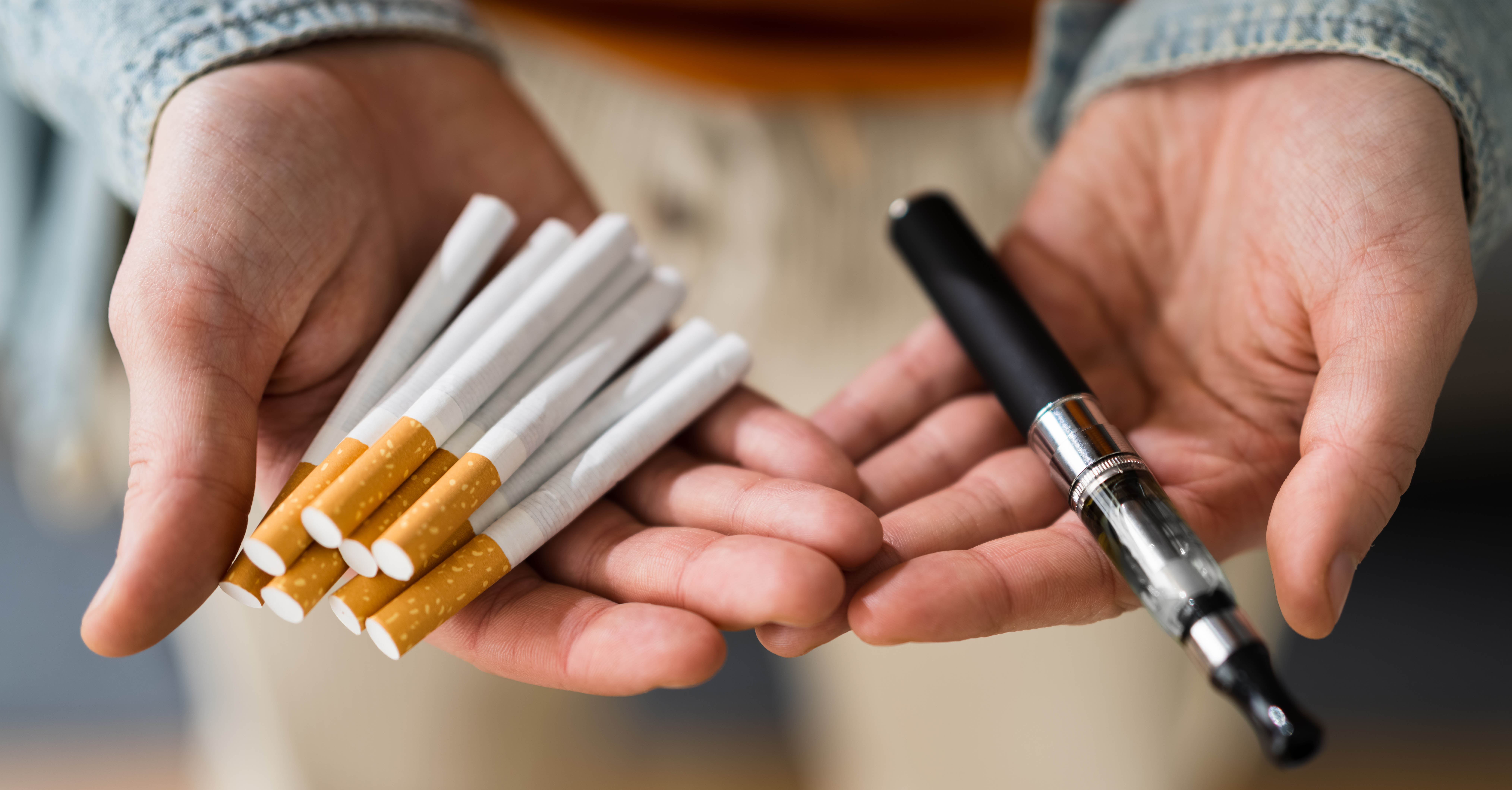 A person holding cigarettes in one hand and e-cigarettes in the other.
