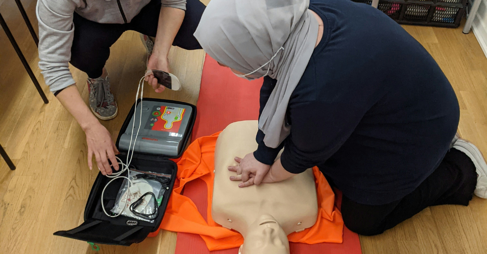 Two people conduct CPR training chest compressions on a CPR Manikin