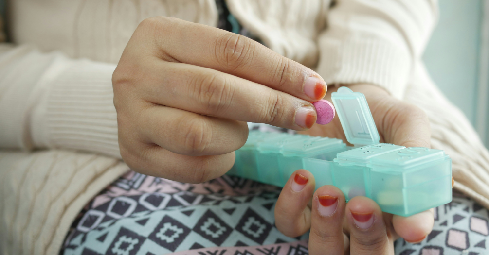 An elder woman taking a pill from a pill organizer.