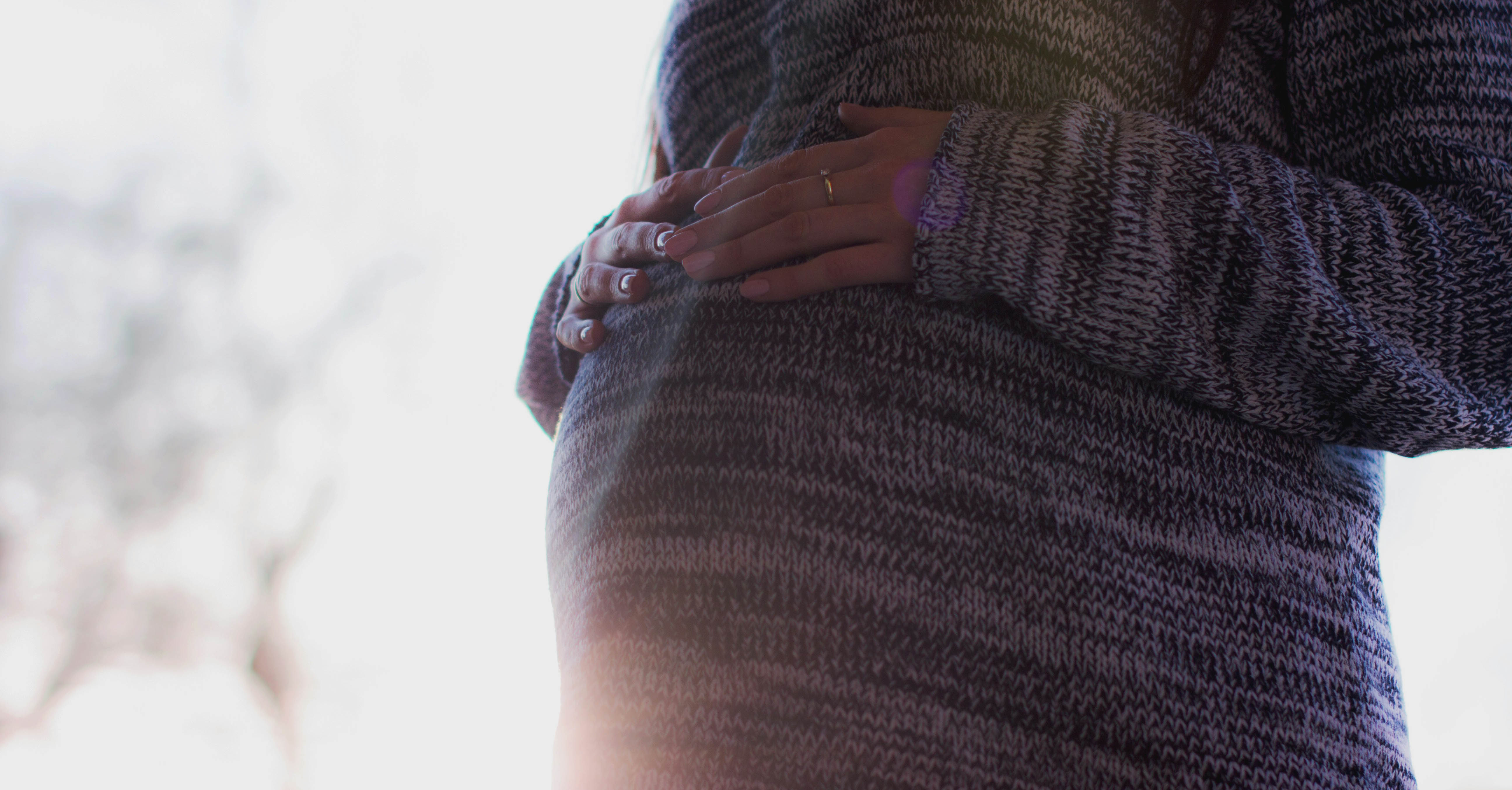 A pregnant person puts their hands on their stomach.