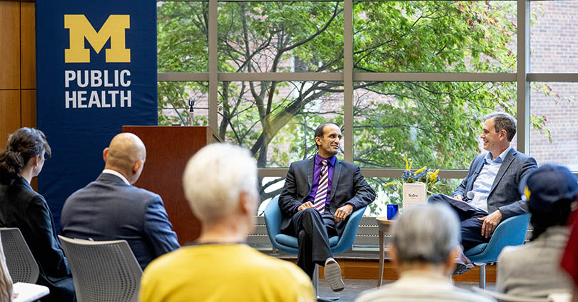 Raj Panjabi and Dean Charles B. Holmes walk in front of an audience in the Cornely Community Room