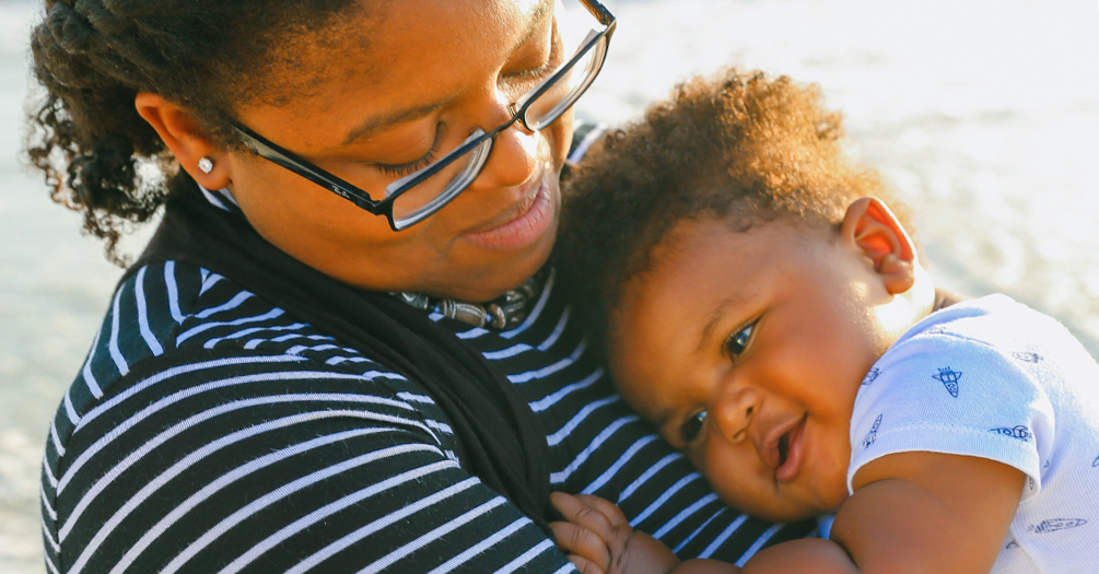 A black mother stands on a beach while holding her infant