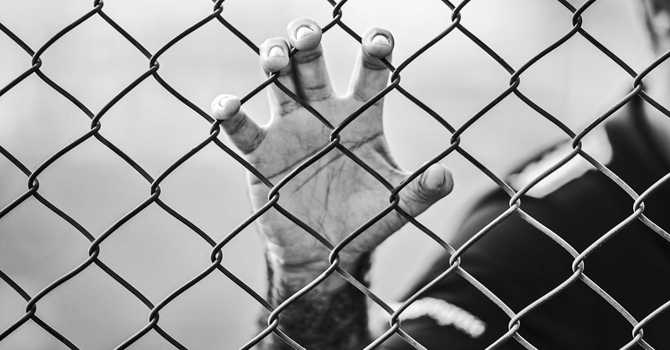 An imprisoned person grips a chain-link fence