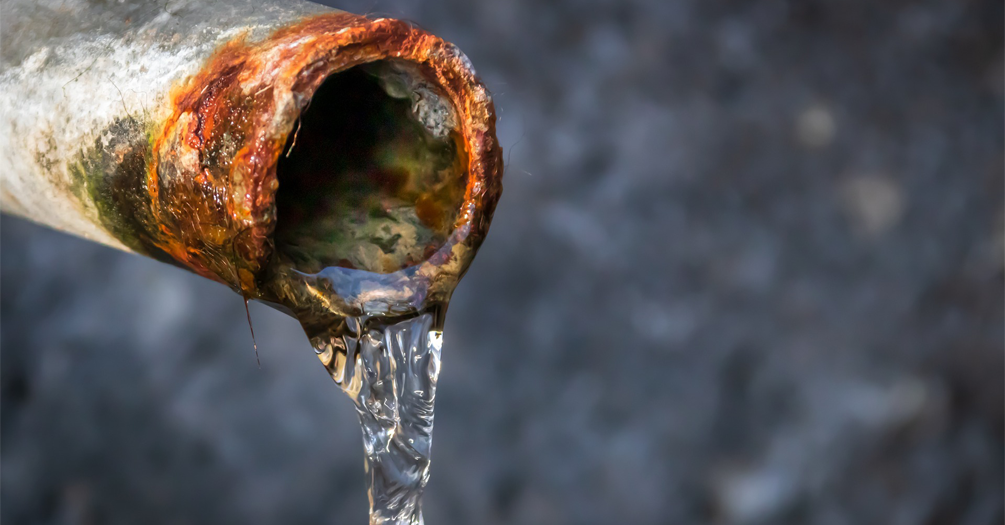 Water trickles out of the end of a rusty pipe