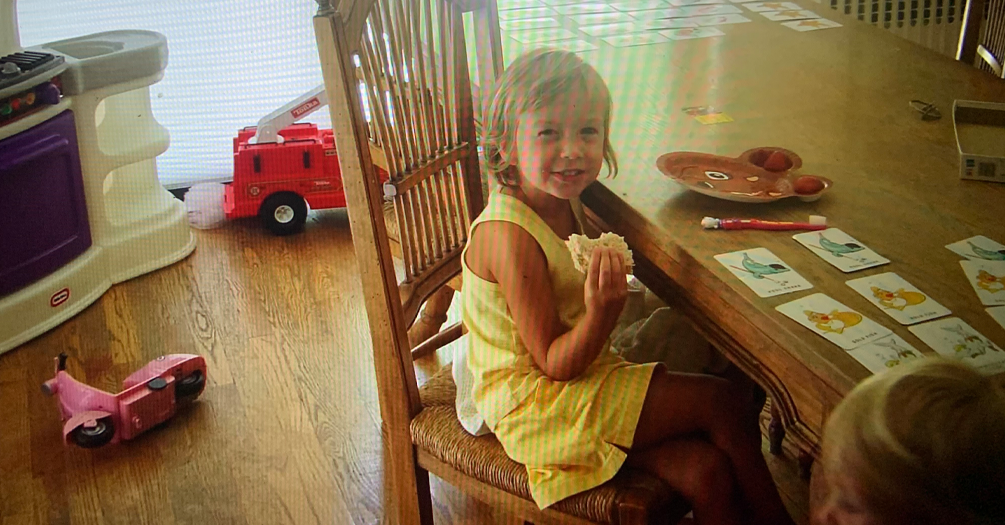 Childhood photo of the author sitting at table eating a sandwich.