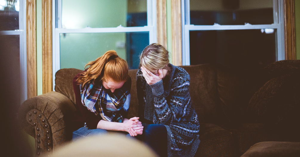 Two women sit on a couch while in emotional distress and grieving