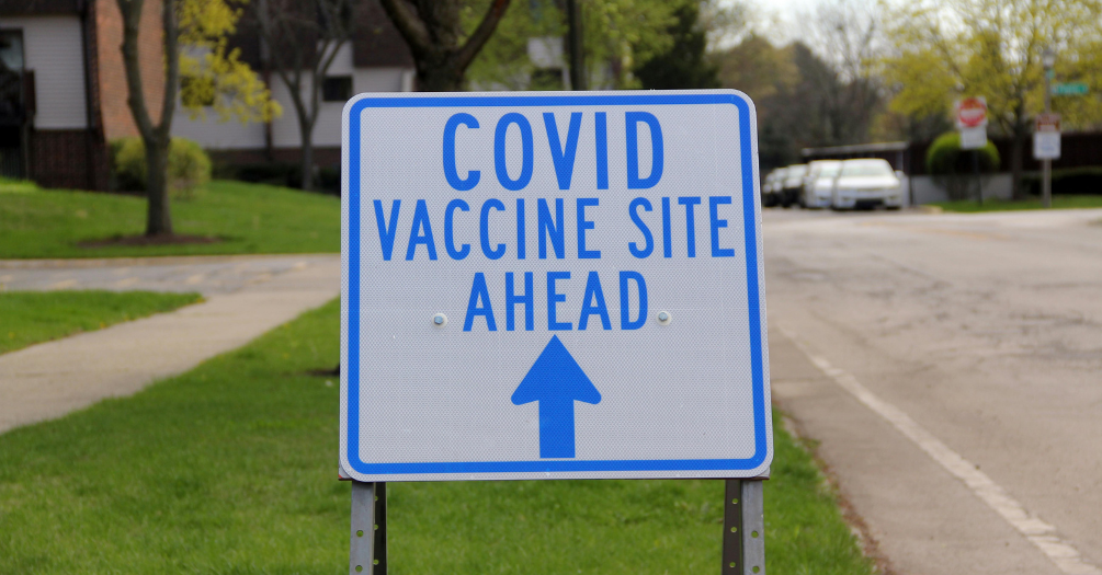 A large sign that reads "COVID Vaccine Sign ahead" in a neighborhood