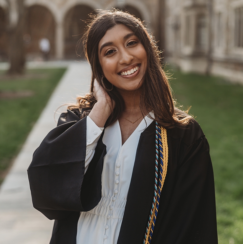 Sania Farooq in her graduation gown posing in front of the University of Michigan Law School.