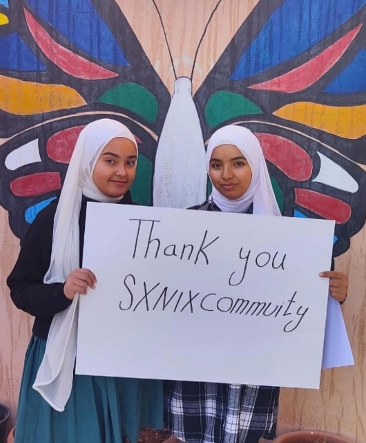 Two members of the Azraq Youth Foundation hold up a sign that reads "Thank you Sxnix Community."