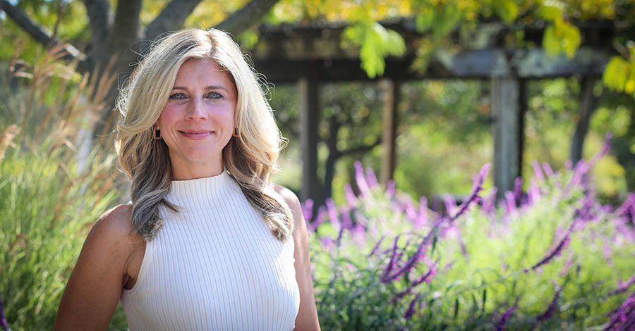 Nicolle Marinec with a white sleeveless shirt standing in front of purple flowers